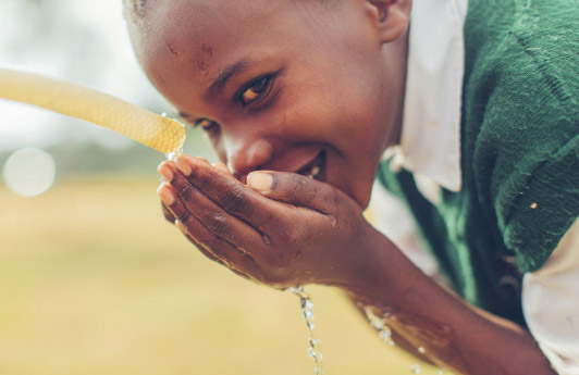 A smiling child drinks water from a hose